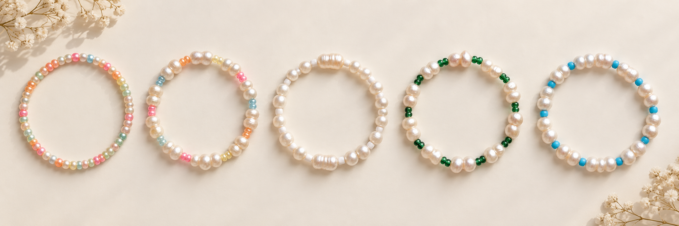 Five pearl and colorful bead anklets arranged on an ivory background with delicate flowers
