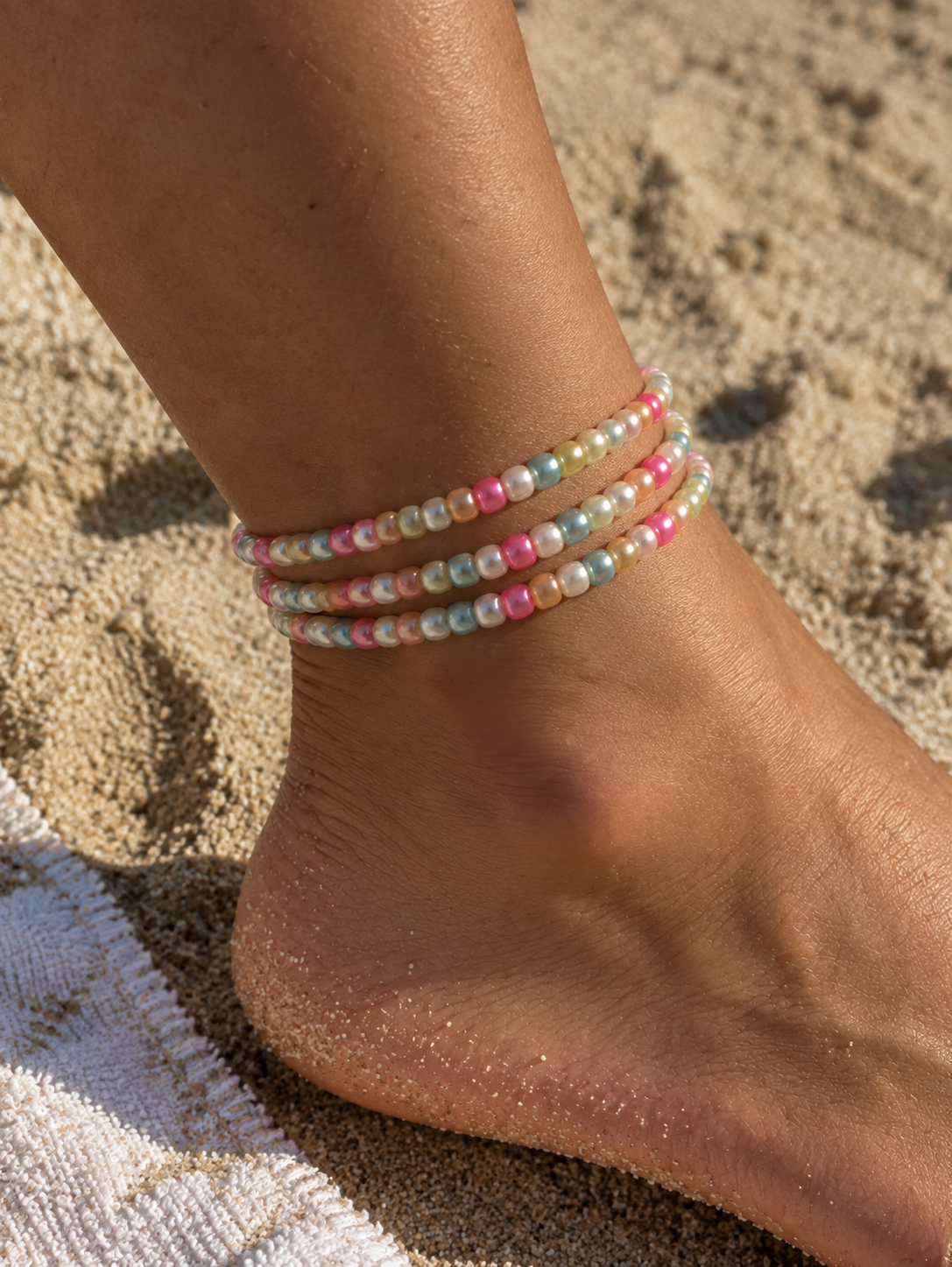 Three colorful bead anklets stacked on an ankle on the beach